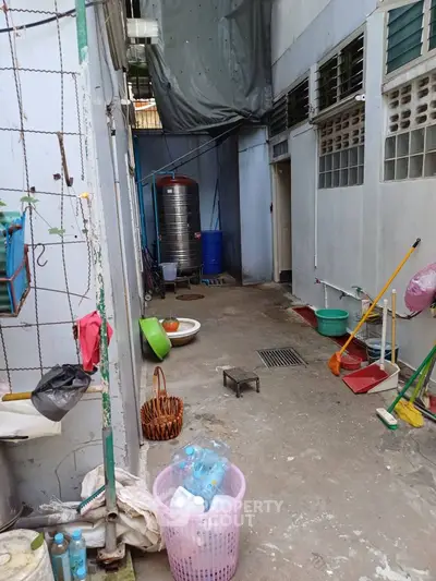 Backyard area with cleaning tools and water storage tank, ideal for utility purposes.