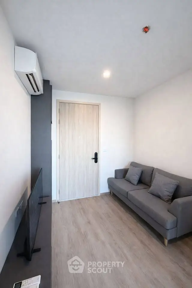 Modern minimalist living room with sleek gray sofa and wall-mounted TV, featuring light wood flooring and neutral tones.