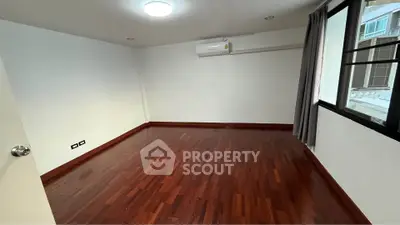 Spacious empty room with wooden flooring and large window in modern apartment.