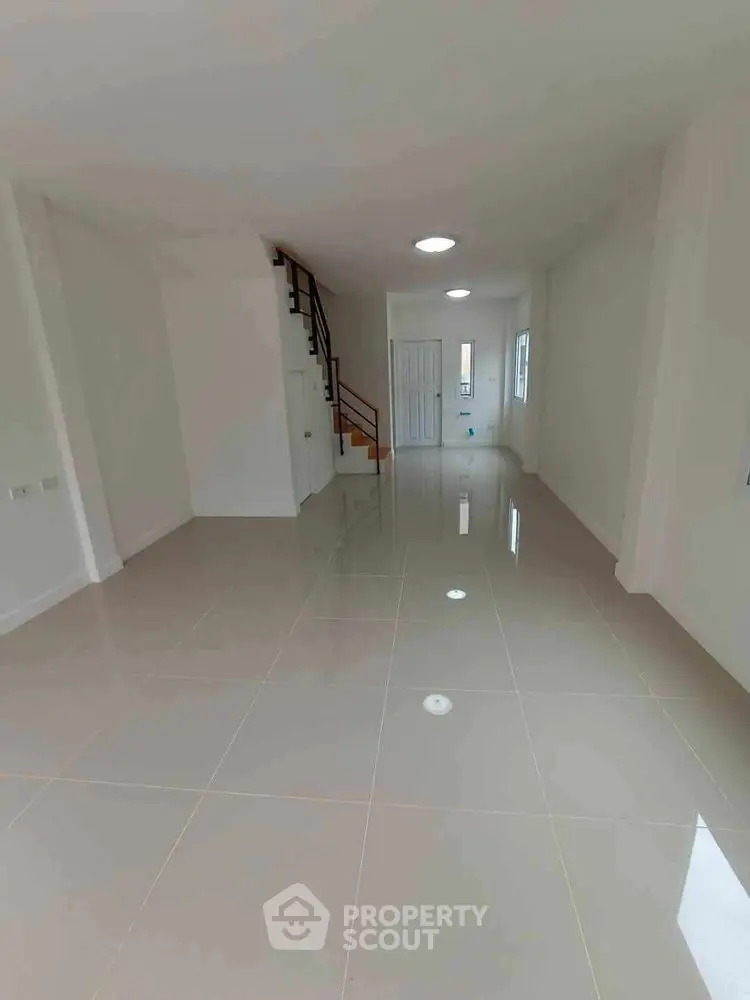 Spacious open-plan living area with glossy tiled floors and staircase.