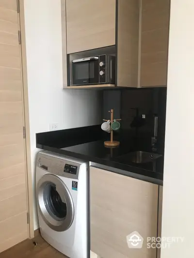 Compact modern kitchenette with built-in microwave, sleek black countertops, and a convenient washing machine, perfect for urban living.