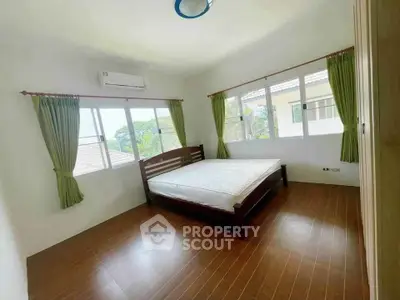 Spacious bedroom with large windows and wooden flooring in a bright, airy home.