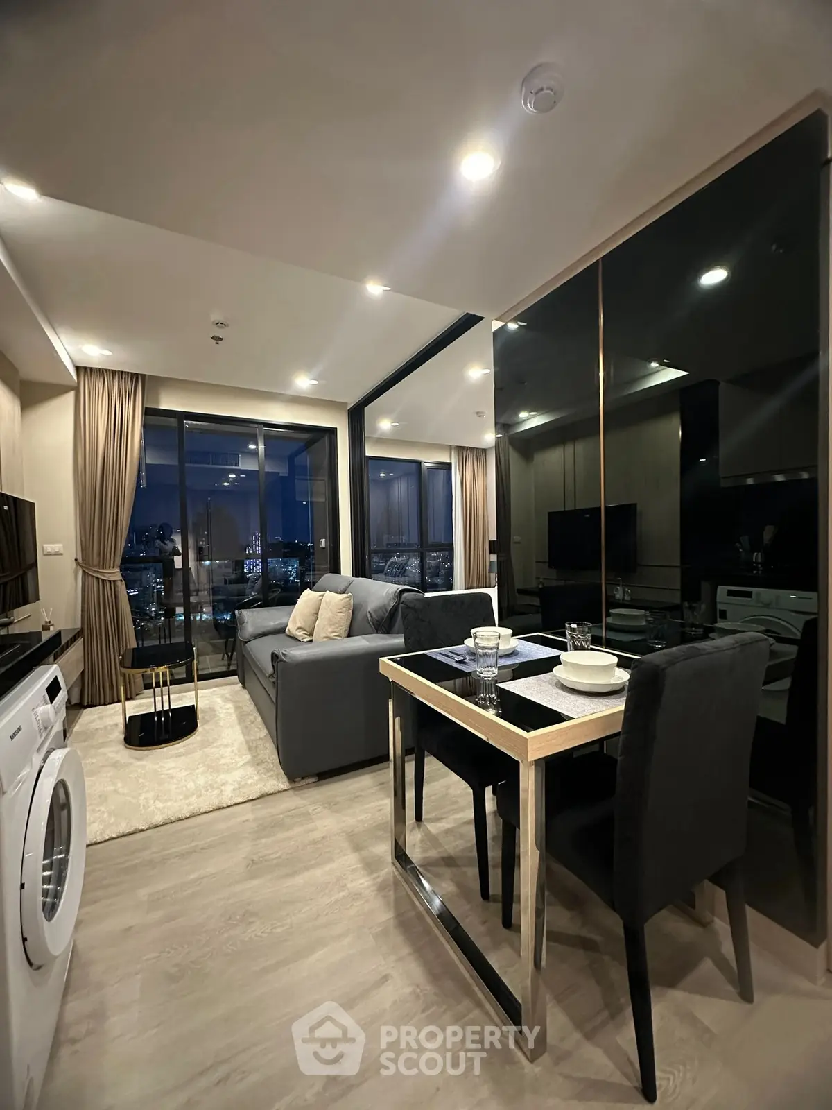 Modern living room with city view, sleek furniture, and washing machine in a stylish apartment.