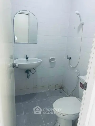 Compact bathroom with white tiles, wall-mounted sink, and shower in minimalist design.