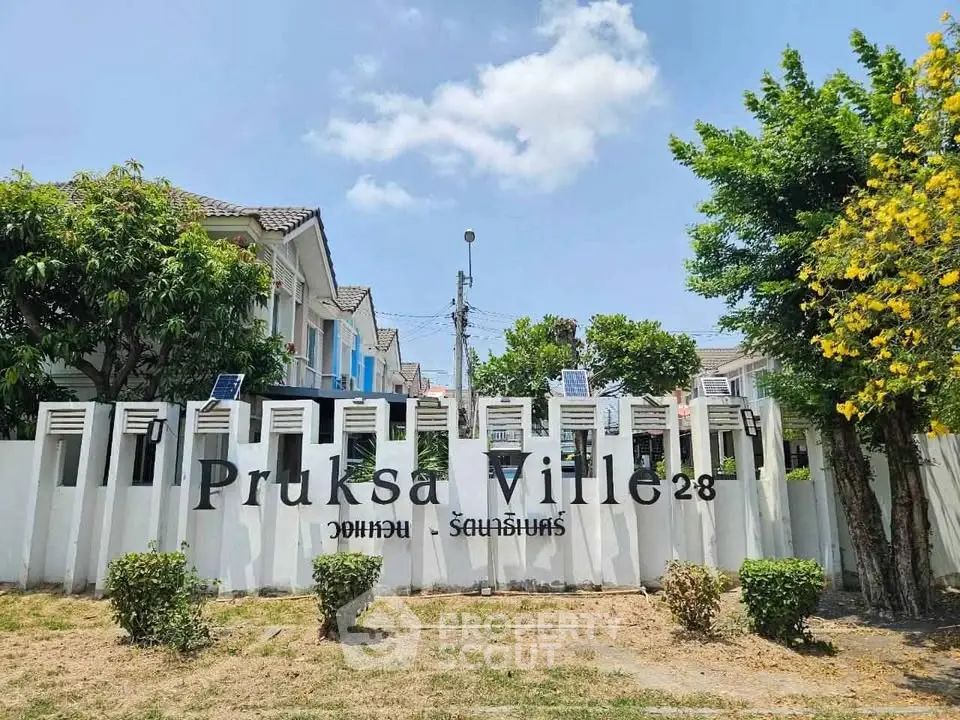 Charming residential community entrance with lush greenery and clear blue sky.