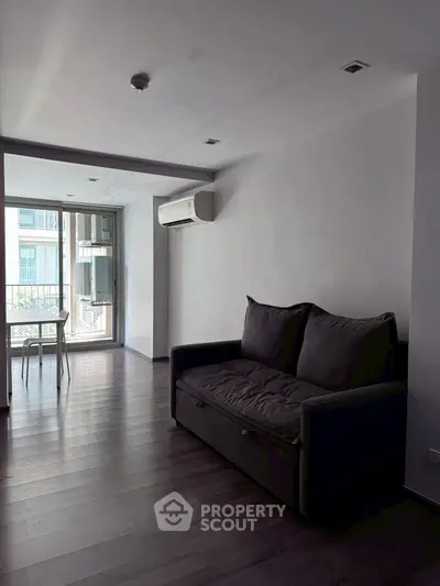 Spacious living room with modern sofa and air conditioning, featuring large windows for natural light.