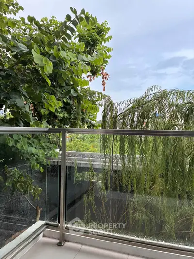 Serene balcony view with lush greenery and glass railing, perfect for relaxation.