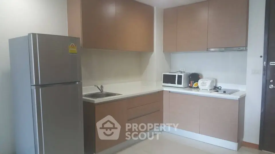 Modern kitchen with sleek cabinets, stainless steel fridge, and microwave in a compact layout.