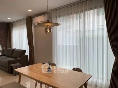 Modern living room with elegant dining area and large windows with sheer curtains.