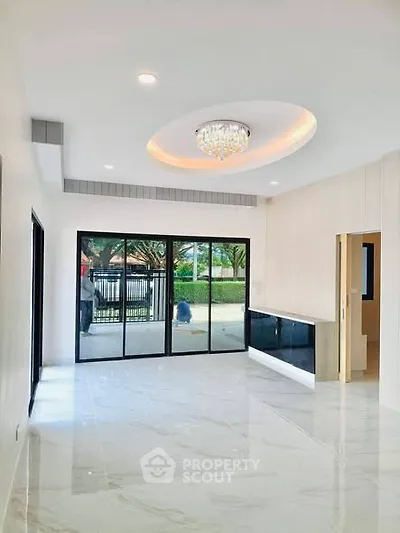 Spacious modern living room with elegant chandelier and large glass doors opening to a garden view.