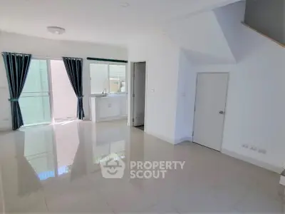 Spacious open-plan living area with glossy tiled floors and natural light, featuring a compact kitchen corner.