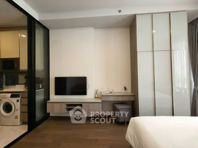 Modern bedroom with sleek TV setup and adjacent kitchen area in a stylish apartment.