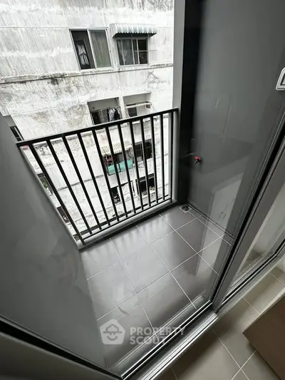 Compact balcony with tiled flooring and metal railing, offering urban views.