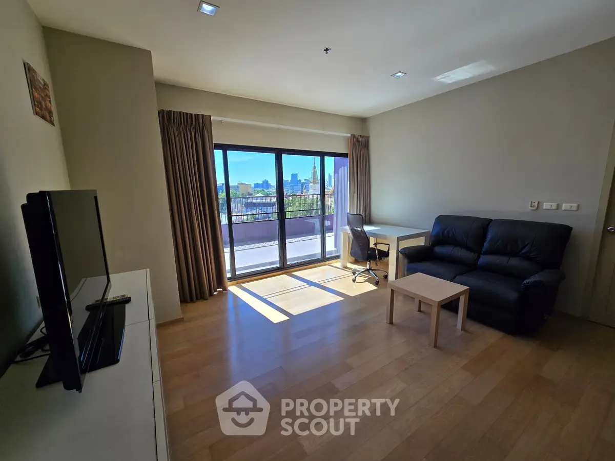 Spacious living room with balcony and city view, featuring modern furniture and natural light.