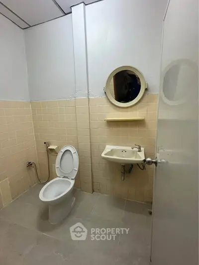 Simple bathroom with toilet, sink, and round mirror in neutral tones.