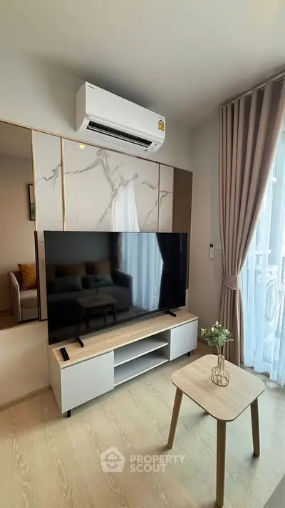 Modern living room with large TV and air conditioning, featuring elegant decor and natural light.