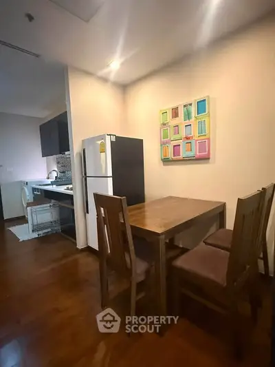 Cozy dining area with wooden table and chairs, adjacent to a modern kitchen with fridge and washing machine.