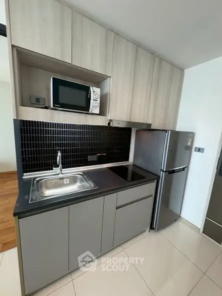 Modern compact kitchen with sleek cabinetry and stainless steel appliances in a stylish apartment.