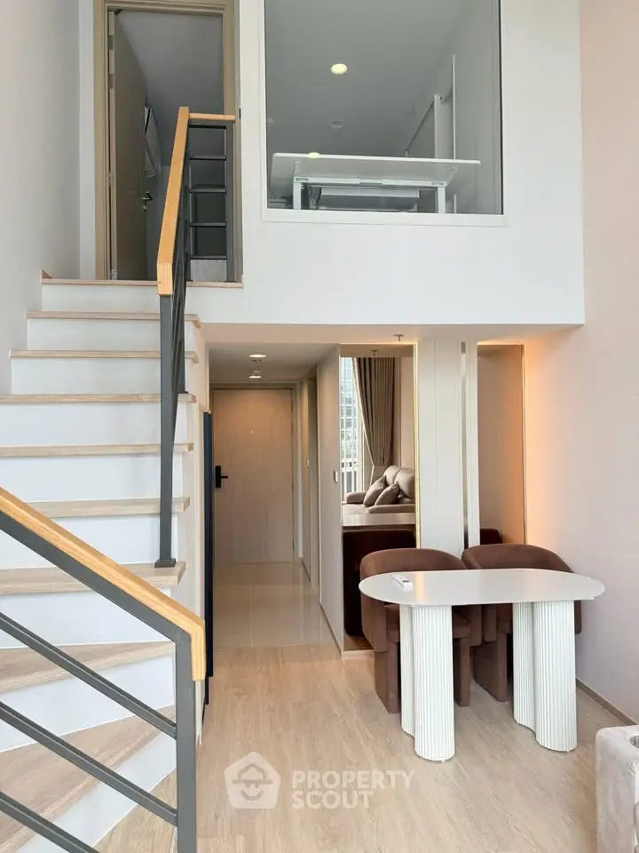 Modern duplex apartment with stylish staircase and open living area, featuring elegant furniture and natural light.