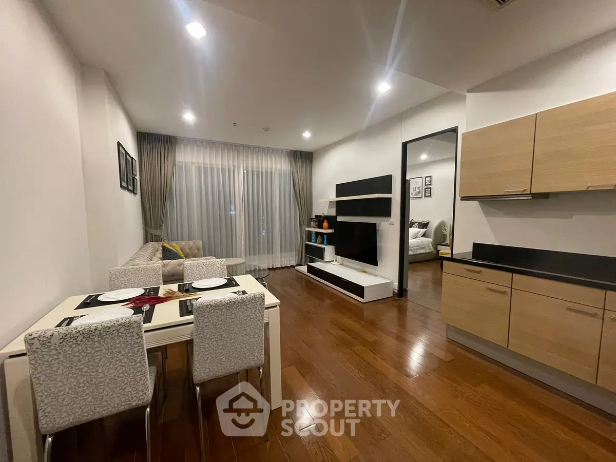 Modern open-plan living room with dining area and kitchen, featuring sleek wooden flooring and contemporary furnishings.