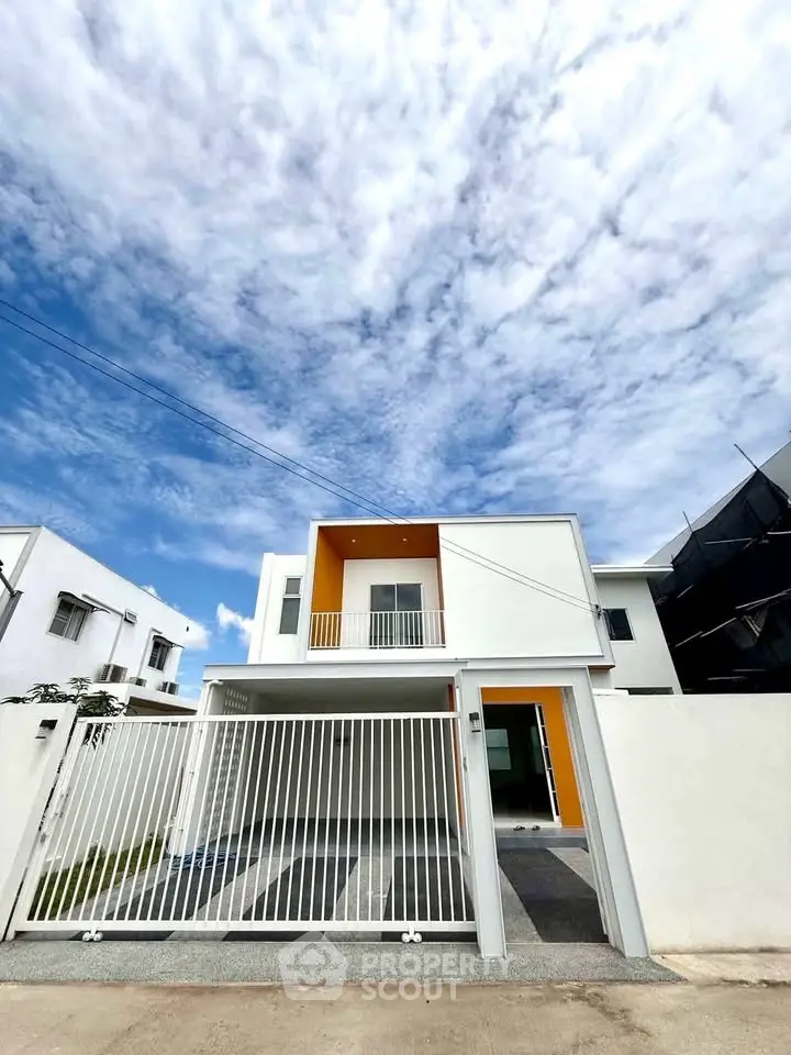 Modern two-story house with sleek design and gated entrance under a vibrant blue sky.