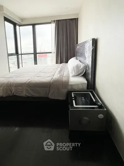 Modern bedroom with large windows offering stunning city views, featuring a cozy bed and sleek side table.