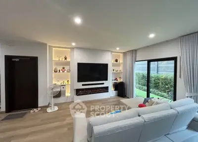 Modern living room with large TV, cozy sofa, and garden view through sliding doors.