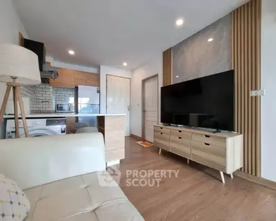 Modern living room with open kitchen, featuring sleek wooden furniture and a large flat-screen TV.