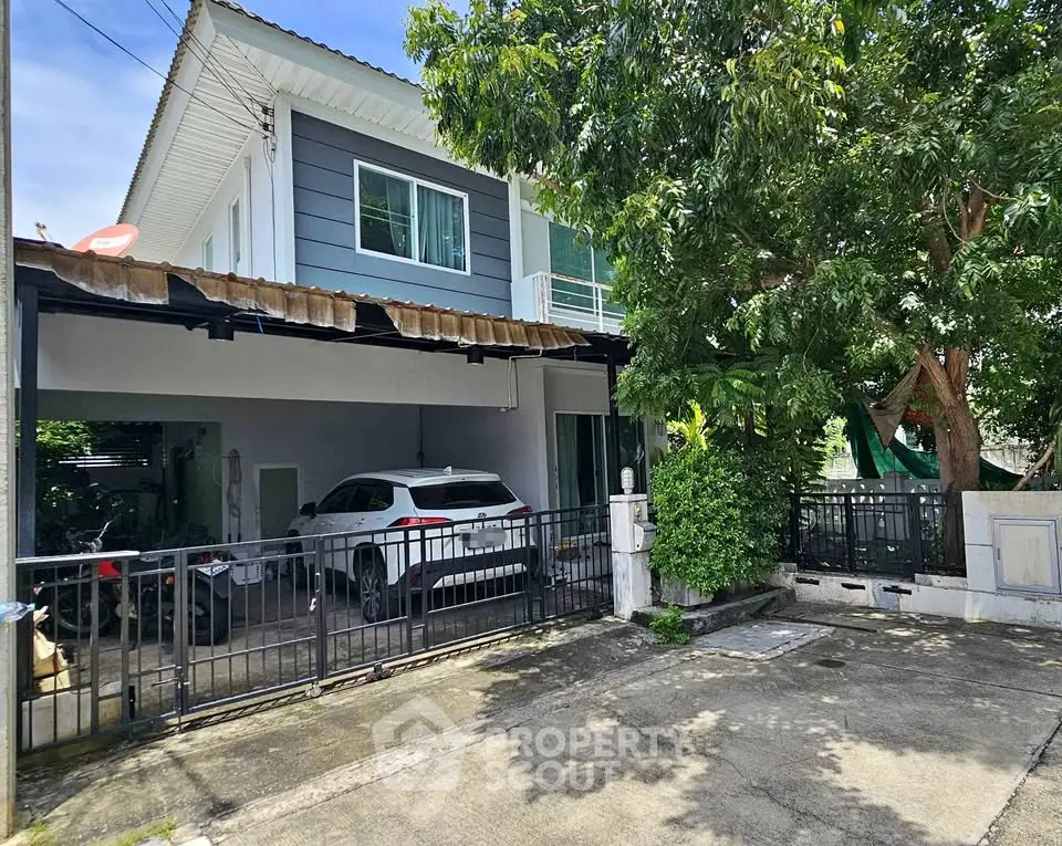 Charming two-story house with carport and lush greenery in a serene neighborhood.