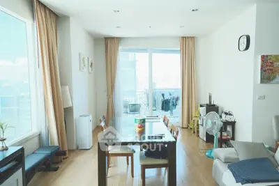 Spacious living room with large windows and balcony access, featuring modern furniture and natural light.