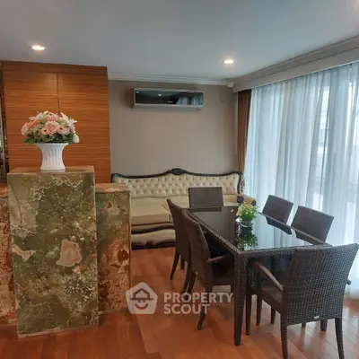 Elegant dining area with wicker chairs and glass table, featuring a plush sofa and floral centerpiece.