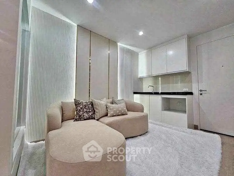 Modern living room with cozy beige sofa and sleek kitchenette in open layout design.