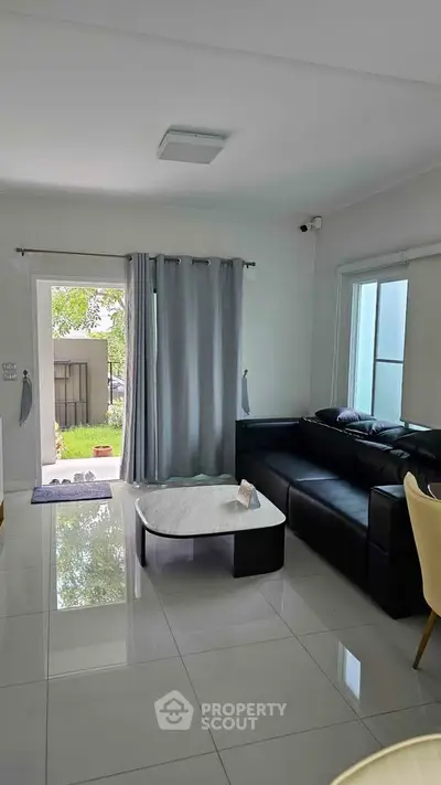 Modern living room with sleek black sofa and marble coffee table, opening to a lush garden view.