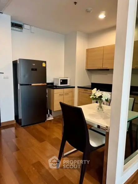 Modern kitchen with wooden cabinets, sleek fridge, and dining area in a stylish apartment.