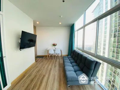 Modern living room with large windows, sleek sofa, wall-mounted TV, and dining area in a high-rise apartment.