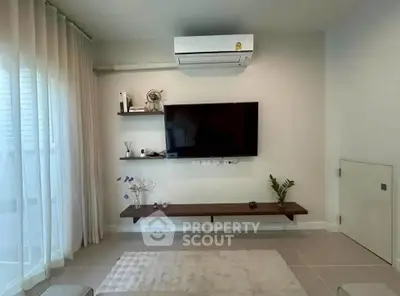 Modern living room with wall-mounted TV and air conditioning, featuring minimalist decor and natural light.