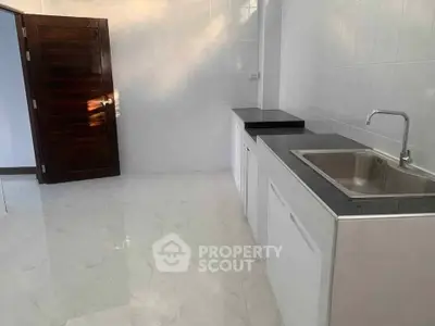 Modern kitchen with sleek countertops and stainless steel sink, featuring a minimalist design and glossy floor tiles.