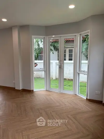Spacious living room with large windows and garden view, featuring elegant wooden flooring.