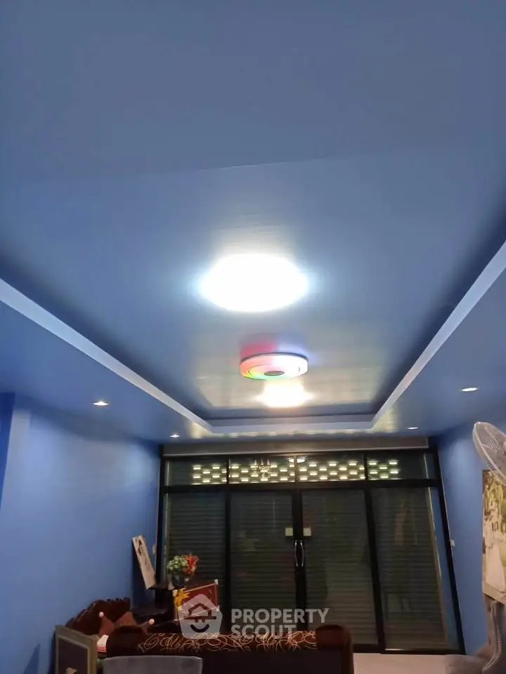 Modern living room with blue walls and ceiling, featuring stylish lighting and large glass doors.