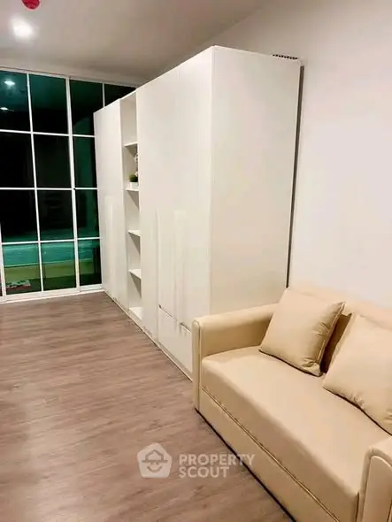 Modern living room with sleek white cabinetry and cozy beige sofa, featuring floor-to-ceiling windows.