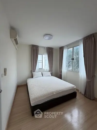 Spacious bedroom with large windows and elegant curtains, featuring a comfortable bed and air conditioning.