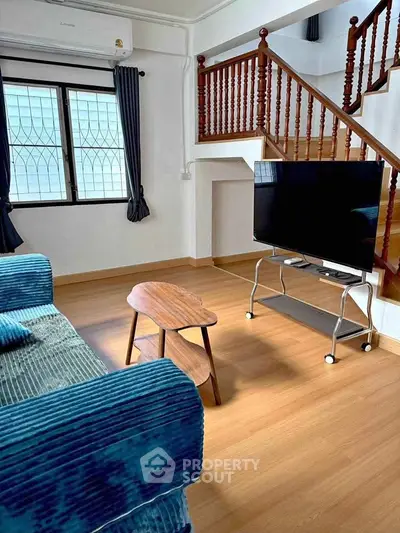 Cozy living room with blue sofa, wooden coffee table, and TV near staircase.