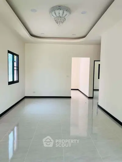 Spacious unfurnished living room with elegant chandelier and tiled flooring.