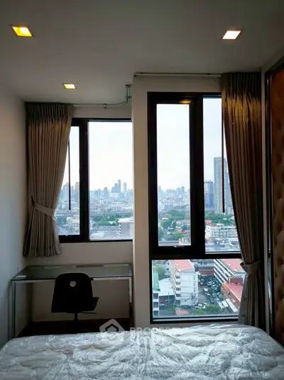 Modern bedroom with stunning city view from large windows, featuring a sleek desk and chair.