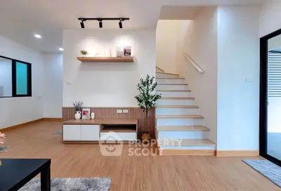Modern living room with stylish decor and wooden flooring, featuring a staircase and built-in shelving.