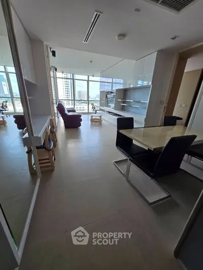 Spacious modern living room with dining area and city view, featuring sleek furniture and large windows.