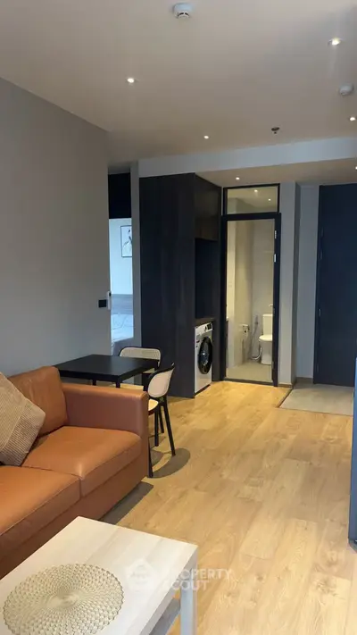 Modern living room with open layout and washing machine, featuring a cozy sofa and dining area.