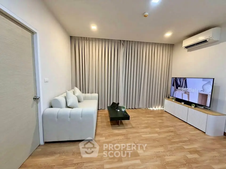 Modern living room with sleek furniture and wooden flooring, featuring a cozy sofa and a flat-screen TV.