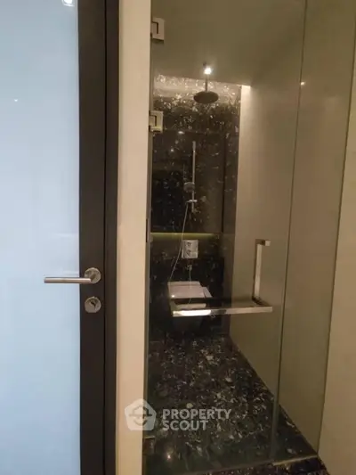 Luxurious modern bathroom with sleek glass shower enclosure and elegant black marble flooring.