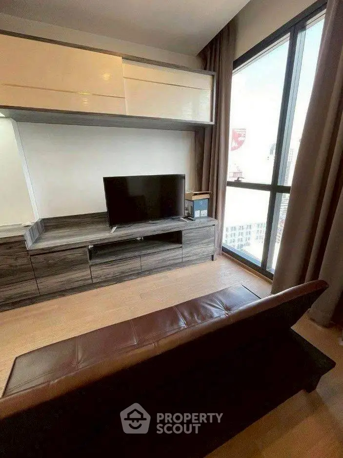 Modern living room with sleek TV unit and large window offering city views.